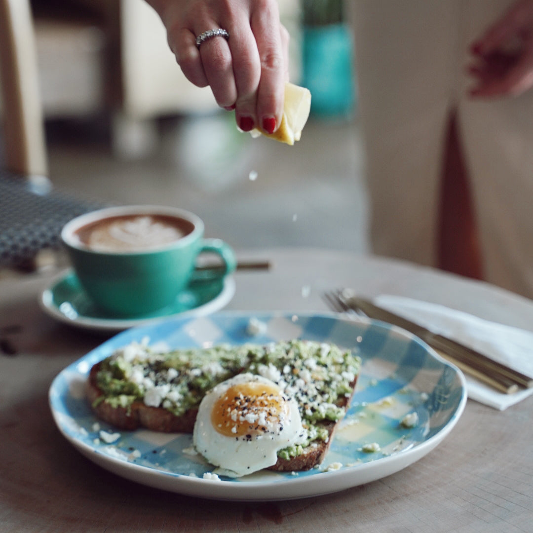 Person seasoning food on a plate with a cup of coffee in the background